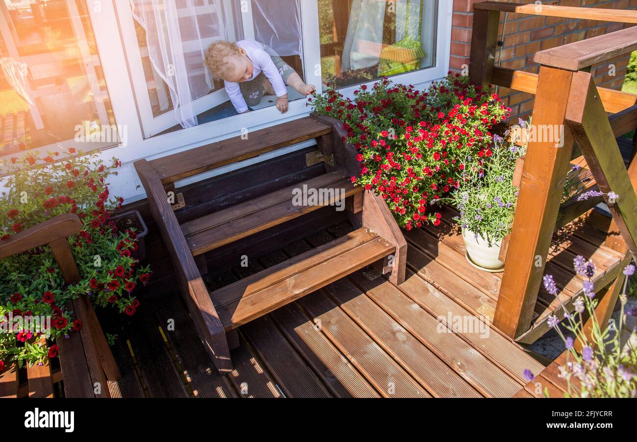 Bambino piccolo che sale su scale di legno balcone, vaso lavanda crescere. Bella giornata di sole. Moderno spazio all'aperto per lo svago. Foto Stock