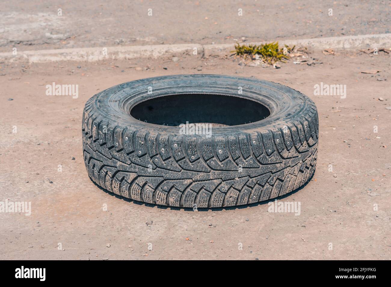 Gettato fuori su una strada deserta, un vecchio pneumatico invernale usurato da una ruota di automobile Foto Stock
