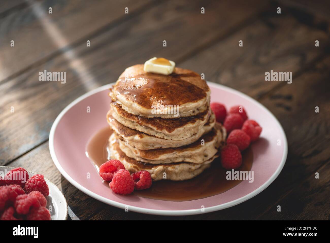 Frittelle di avena con burro, lamponi e sciroppo d'acero su un tavolo di legno. Cibo del mattino Foto Stock