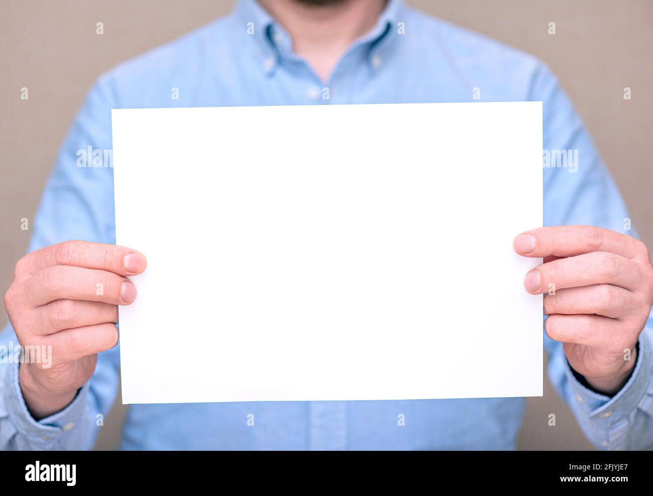 Un uomo in camicia blu, uomo d'affari che tiene foglio bianco vuoto. Spazio per il testo, mockup Foto Stock