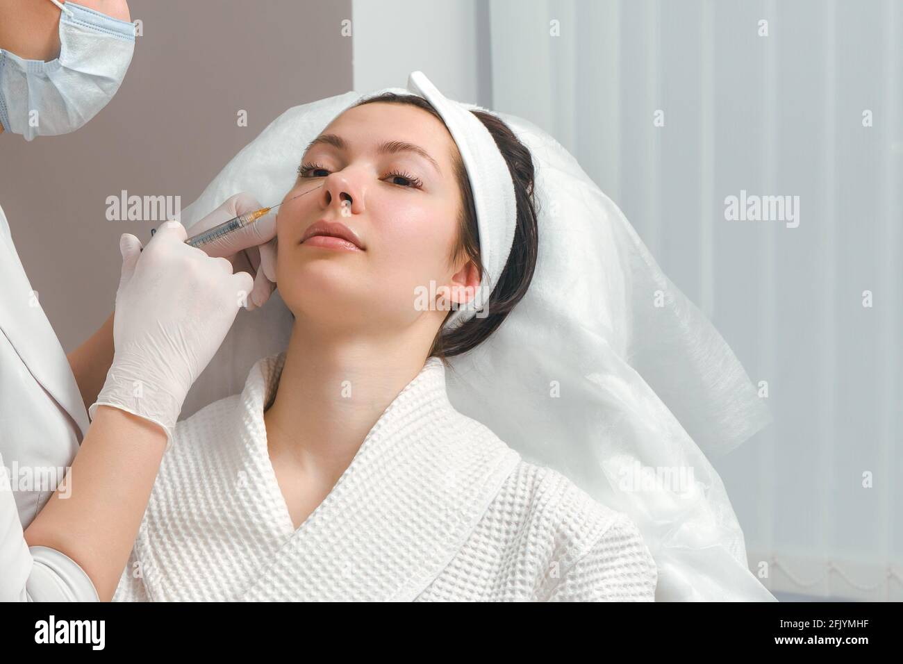 Il dottore cosmetologo rende il ringiovanimento di iniezioni per il viso la procedura di serraggio e levigatura di rughe sulla pelle del viso di una bella Foto Stock