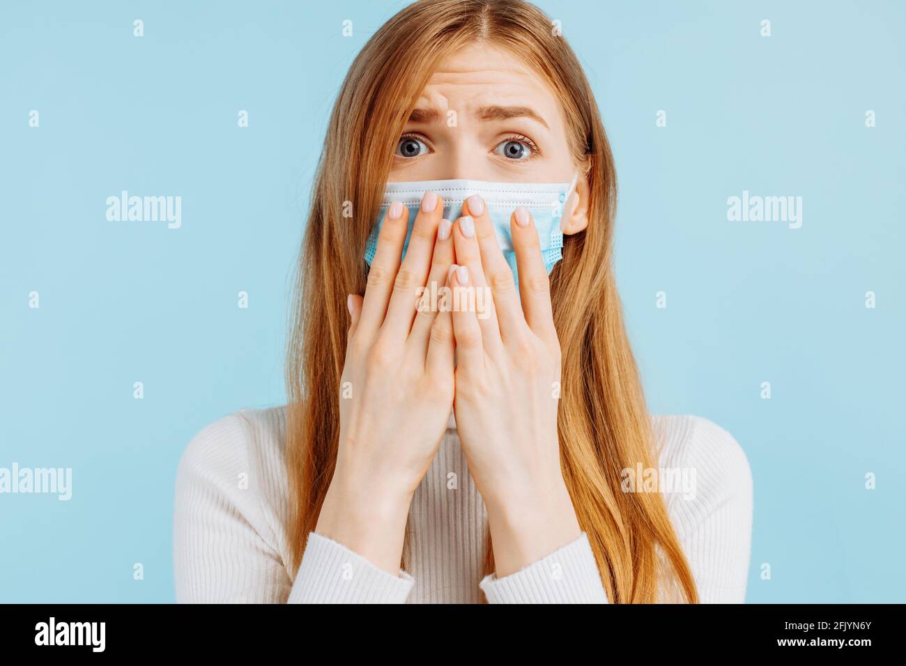 Giovane donna eccitata che guarda gli occhi larghi alla bocca di copertura della macchina fotografica con le mani sullo sfondo blu isolato dello studio con spazio per la copia Foto Stock