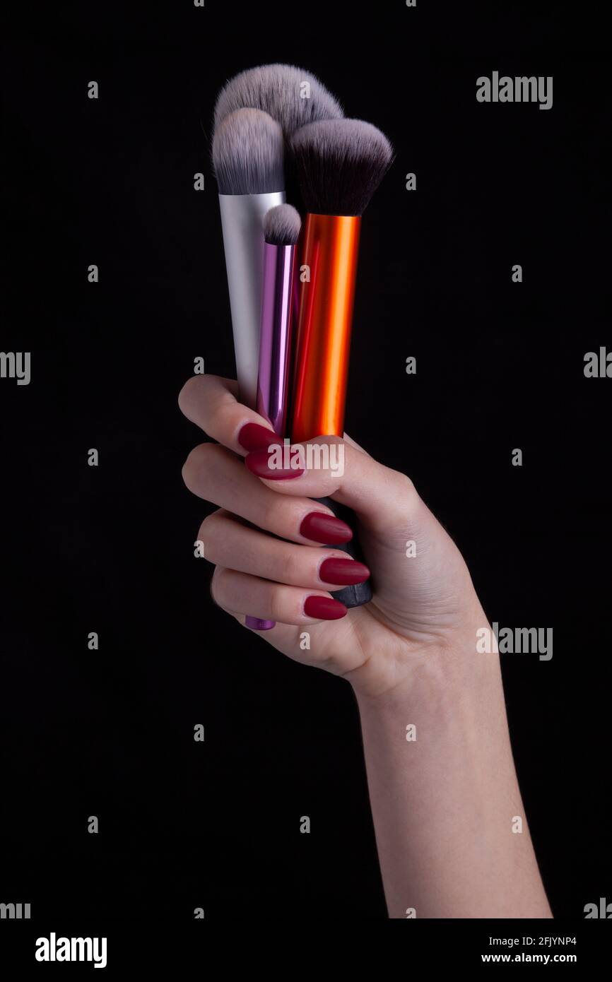 Donna mano che tiene i pennelli del make-up su sfondo blacl Foto Stock