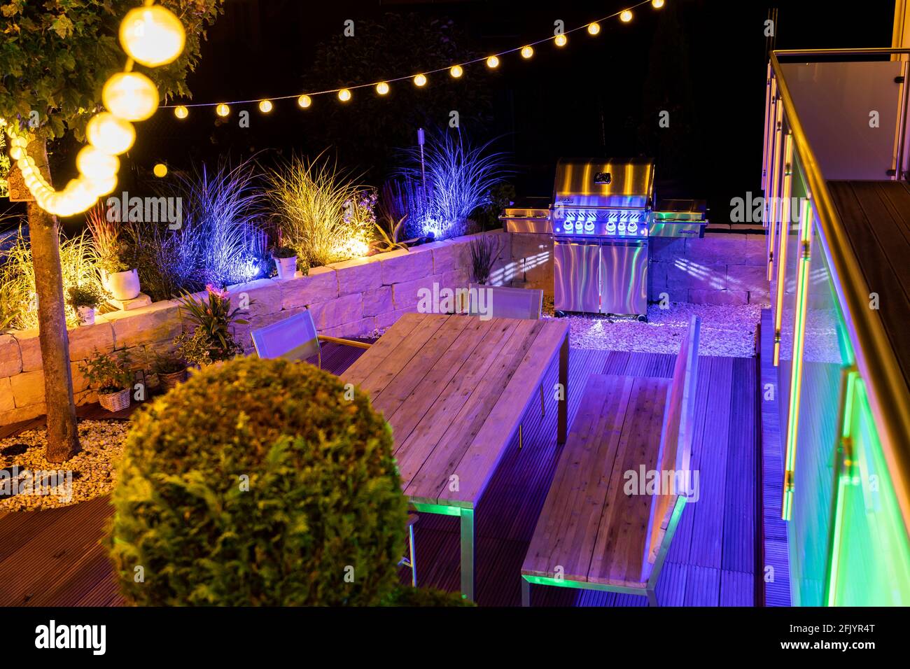 Barbecue a gas su un'elegante terrazza in legno illuminata Foto Stock