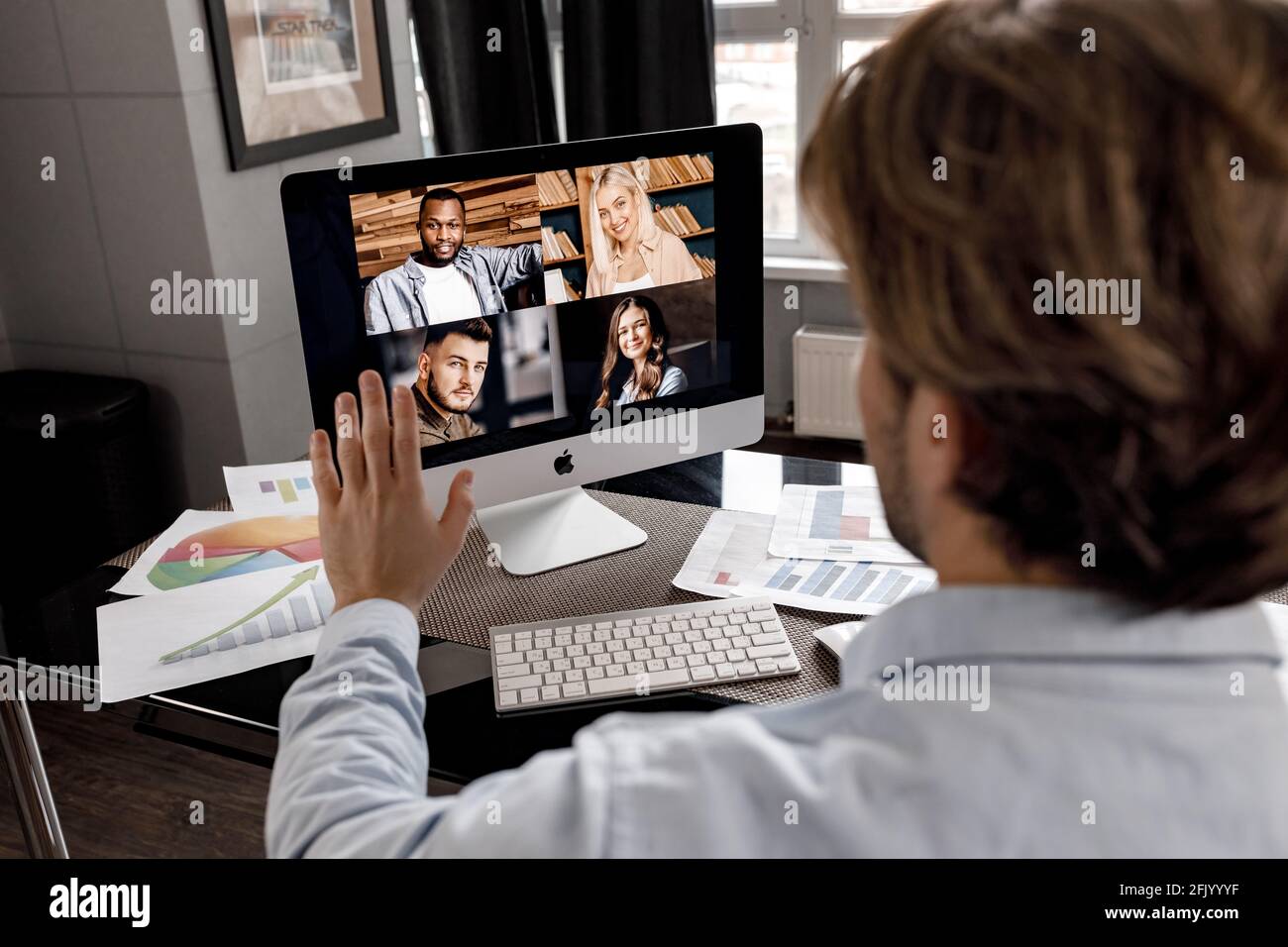 Indietro guarda il ritratto di un uomo d'affari felice che saluta i colleghi durante la videoriunione, seduto alla scrivania dell'ufficio domestico. Il freelance maschile di stile è Foto Stock