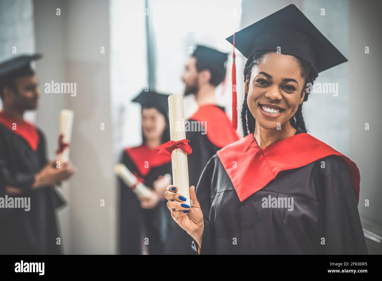 Carino ragazza afroamericana in mortarboard che guarda felice e sorridente bene Foto Stock