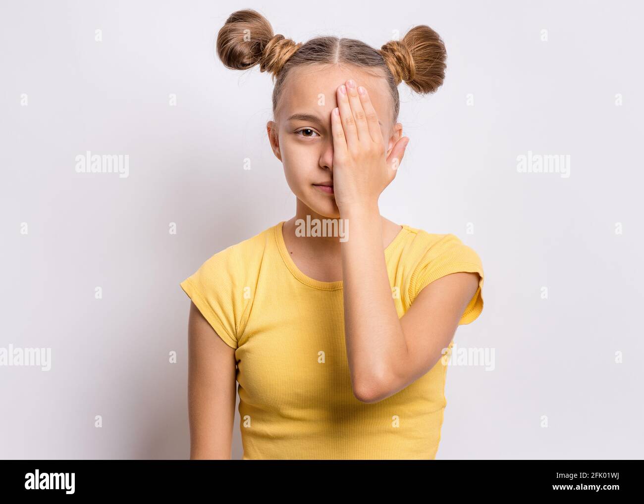 Felice ragazza adolescente guarda con un occhio mentre copre il suo altro occhio con la mano Foto Stock