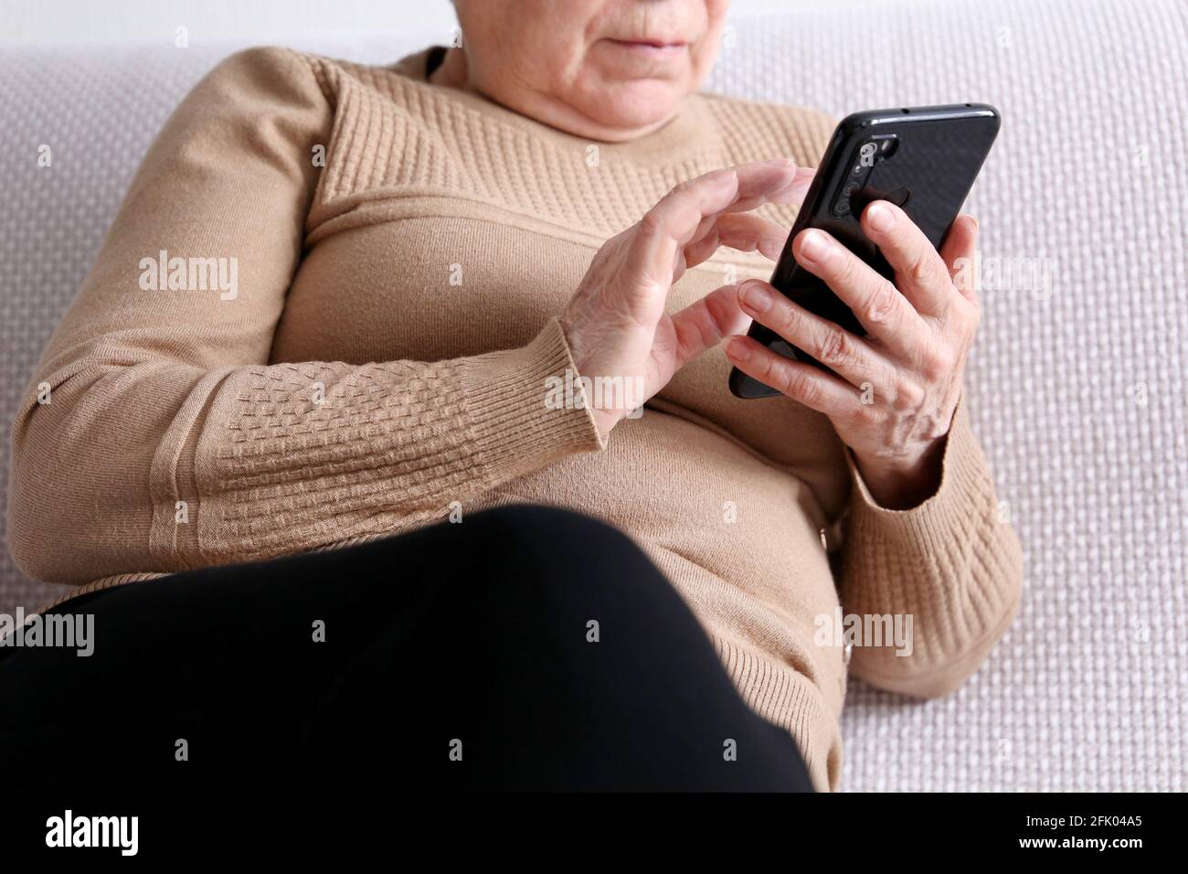 Donna anziana con smartphone seduto sul divano a casa, telefono cellulare in mani femminili. Concetto di comunicazione online in pensione, sms, social media Foto Stock
