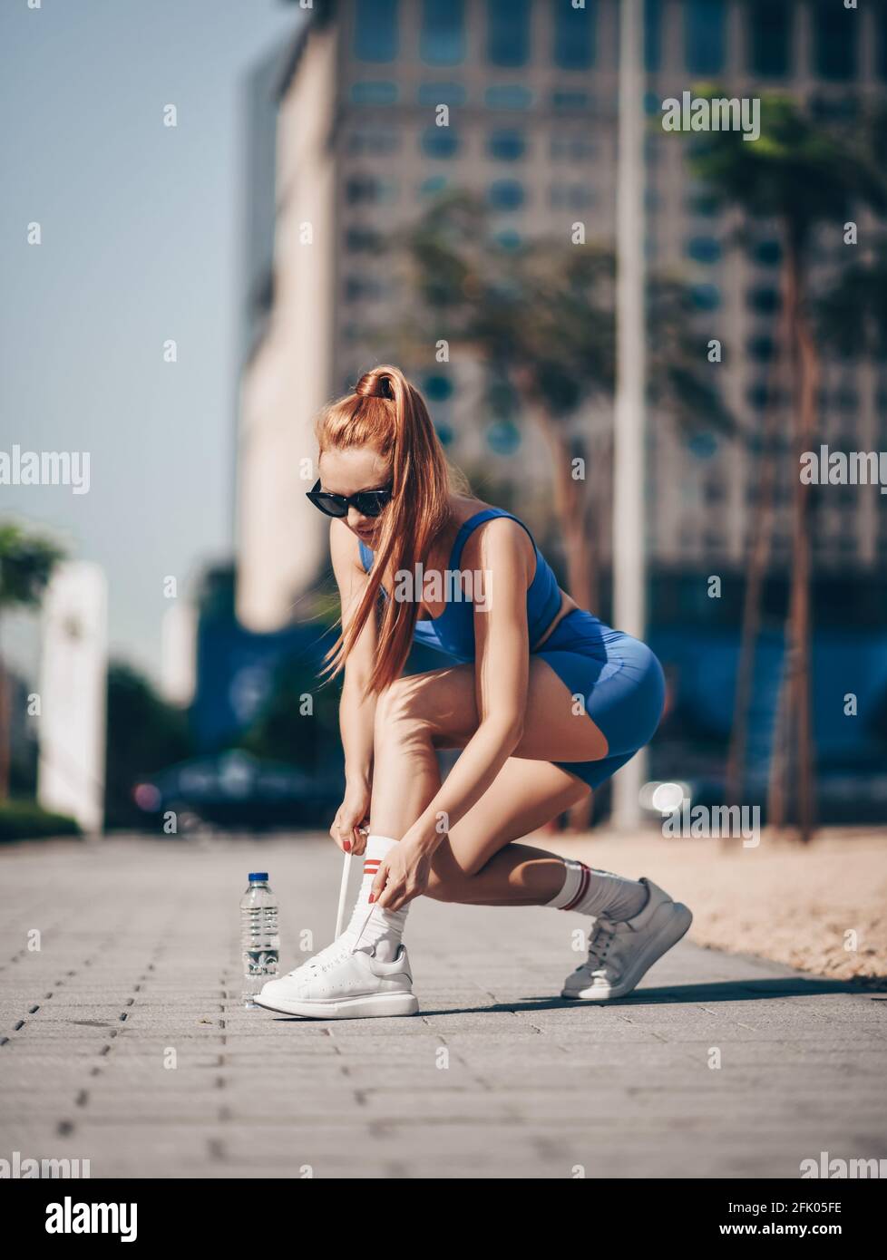 Atleta slim blonde donna trainer corridore in blu sportswear cravatte le sue sneakers prima di allenarsi sulla strada della città Foto Stock