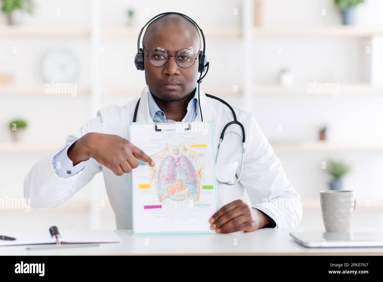 Medico afroamericano che mostra immagine con petto, polmoni e organo respiratorio su blocco note per gli studenti, parlando di malattia di coronavirus su lontano l Foto Stock