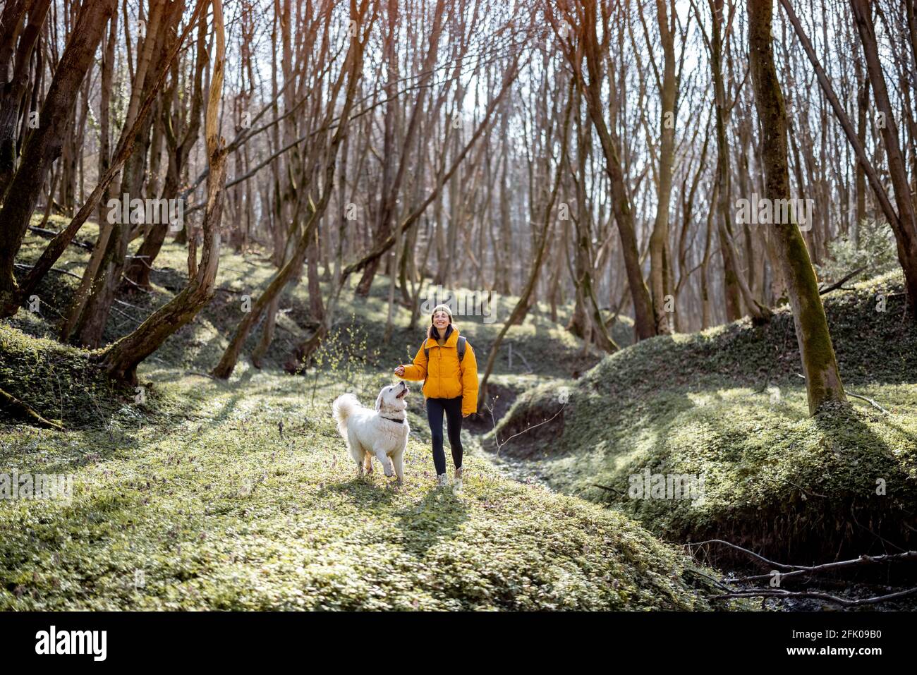 Giovane donna in abiti da trekking e zaino passare il tempo insieme con il grande cane bianco in verde primavera foresta. Gode ed esplora la natura tranquilla. Foto Stock