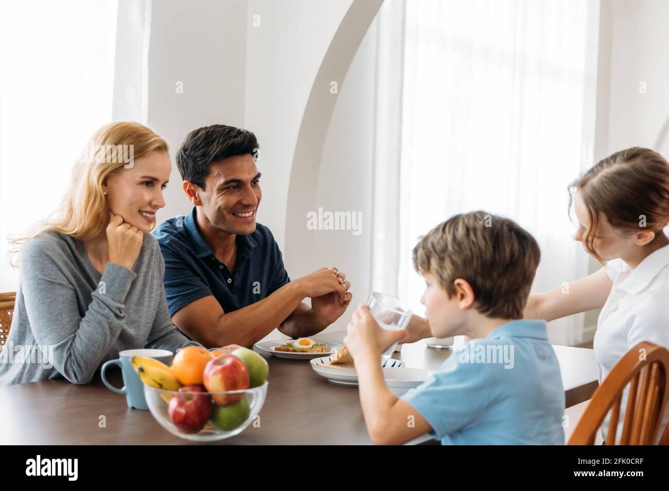 Bella e bella giovane madre sorridente e padre seduto tavolo con figlia e figlio mentre la famiglia godendo sano colazione a casa Foto Stock