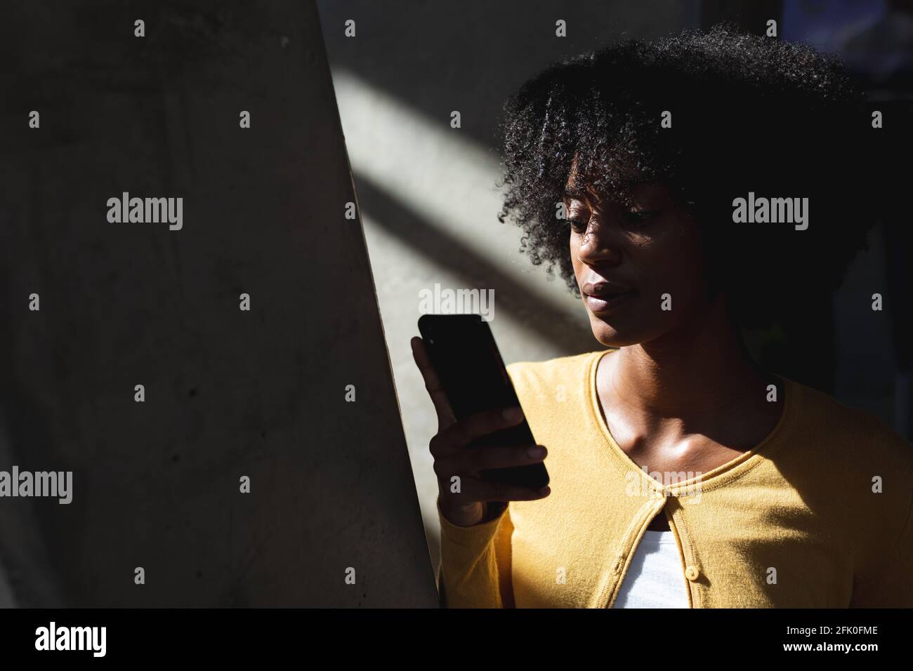 Ritratto di donna afroamericana con smartphone in contrasto elevato interno Foto Stock