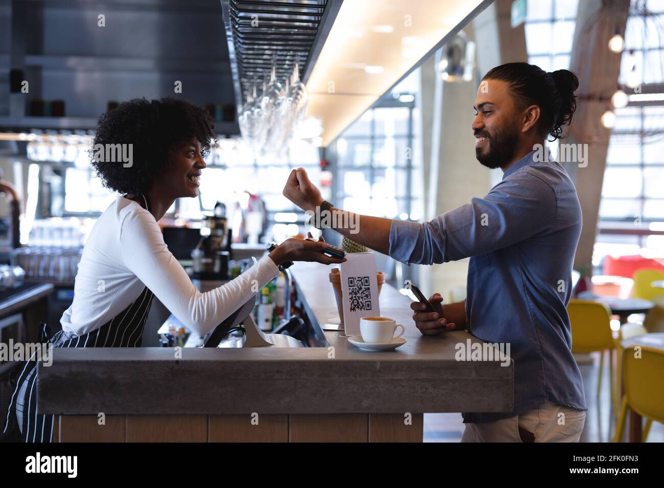 Sorridente cliente misto corsa maschile pagando con smartwatch ad africano barista femminile americana Foto Stock