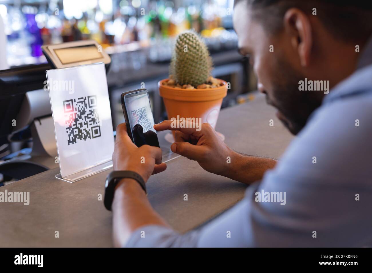 Uomo da corsa misto con smartphone e lettura del codice qr in caffè Foto Stock
