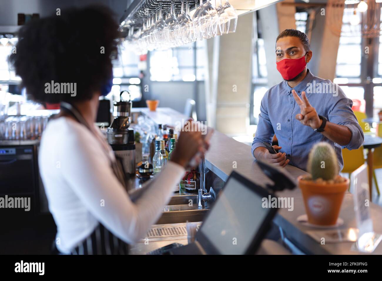 Misto razza cliente maschile indossando maschera viso, ordinando a african american femmina barista Foto Stock