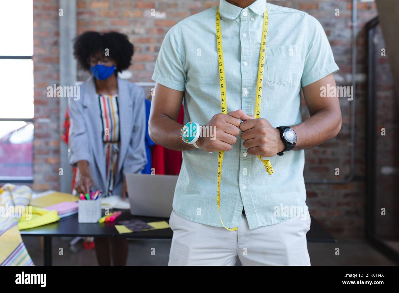 Sezione centrale del progettista misto di corsa che indossa il misuratore del sarto, femmina afroamericana in background Foto Stock