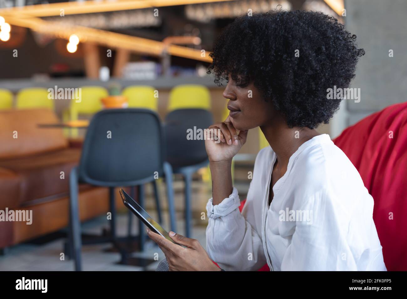 Donna afroamericana seduta sul pouf, usando il tablet nel caffè Foto Stock