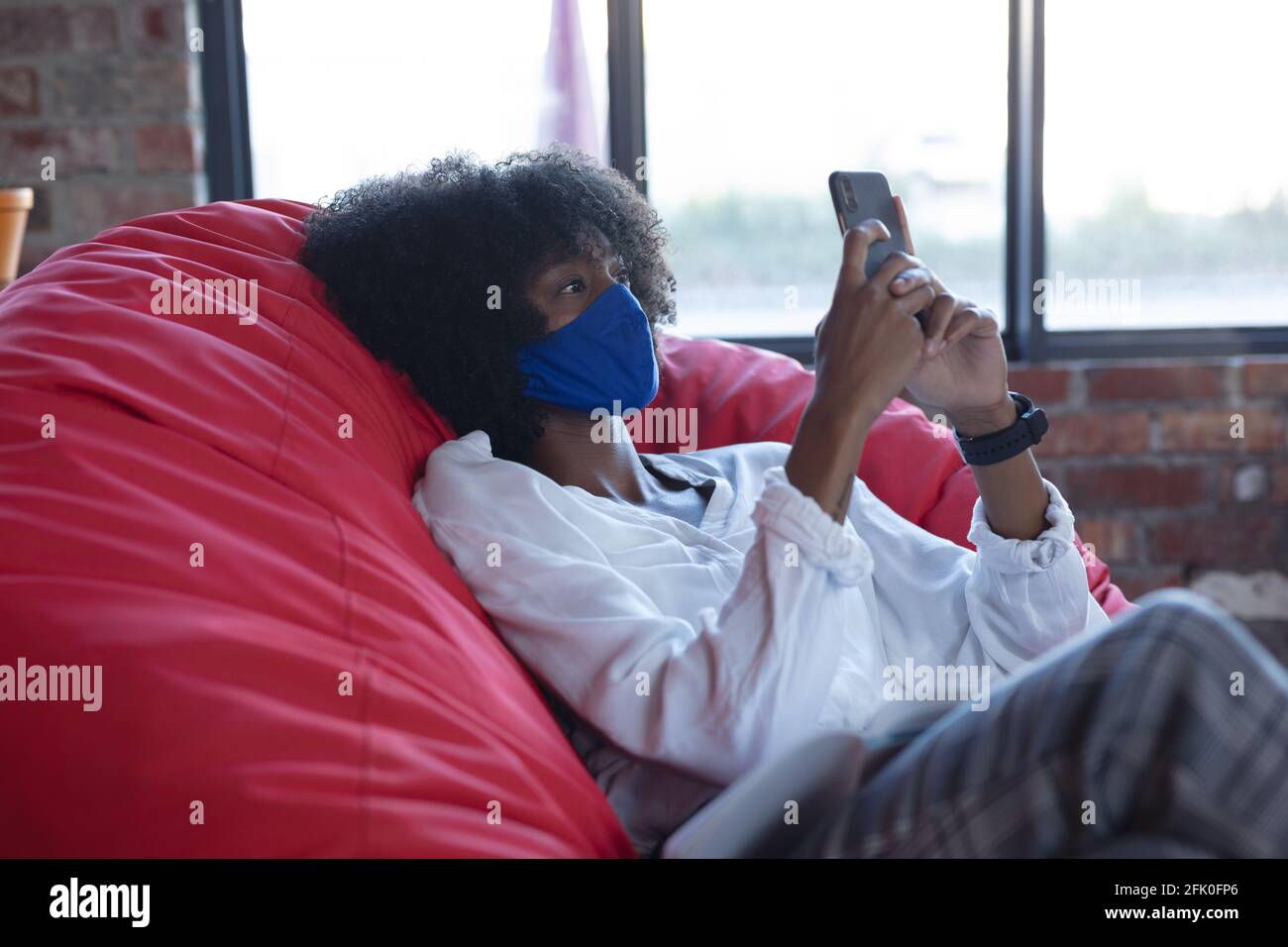 Donna afroamericana che indossa la maschera facciale, seduto, utilizzando lo smartphone al bar Foto Stock