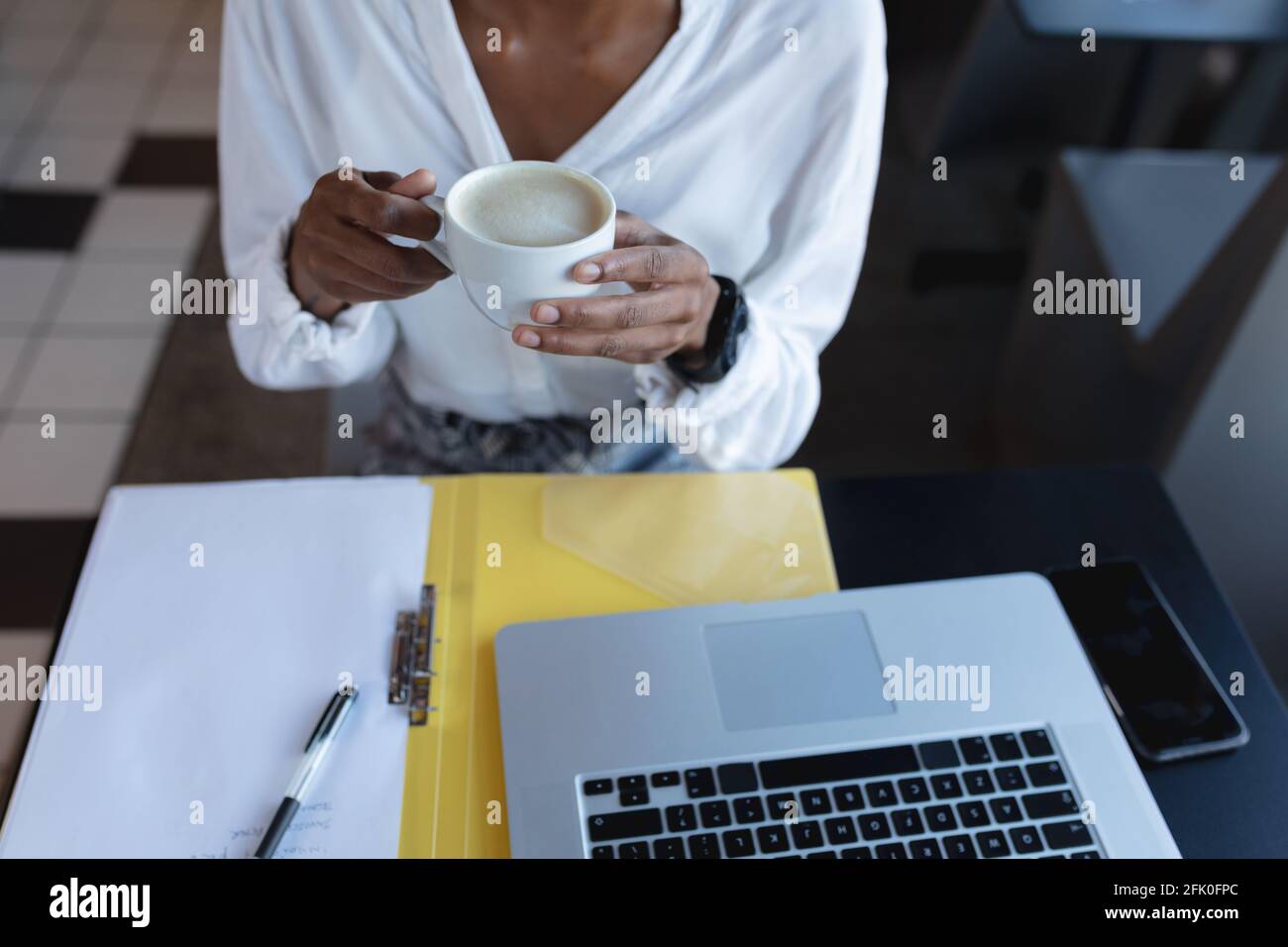 La sezione centrale della donna afroamericana che beve il caffè, usando il laptop e lavorando nel caffè Foto Stock