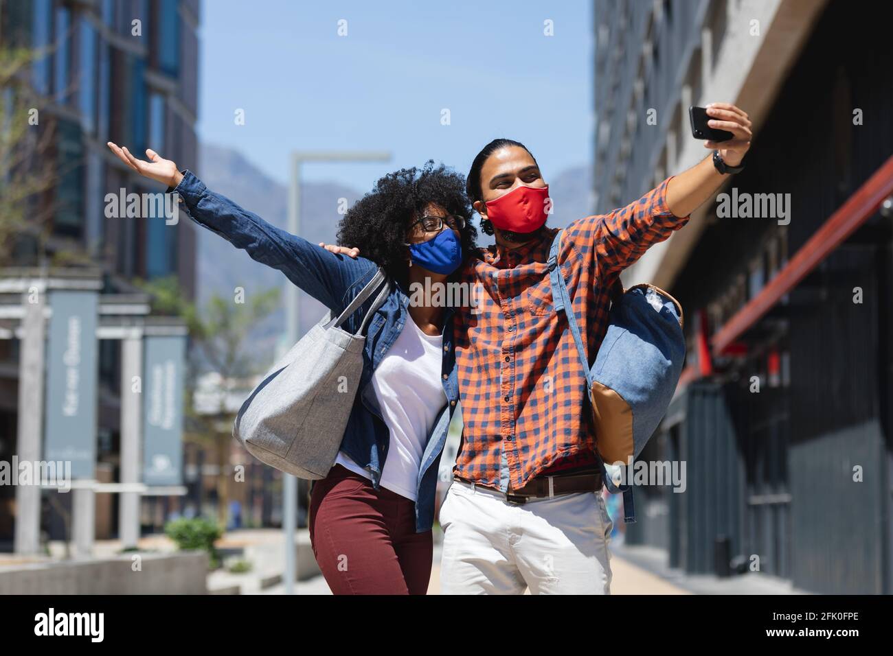 Razza mista uomo e donna afroamericana indossando maschere, abbracciando, prendendo selfie Foto Stock