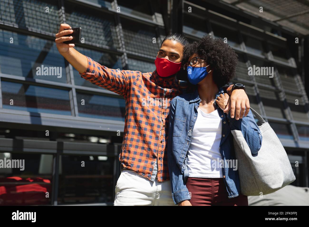 Razza mista uomo e donna afroamericana indossando maschere, abbracciando, prendendo selfie Foto Stock