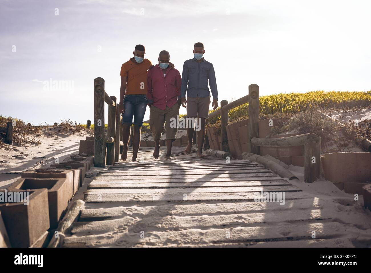 Il padre afroamericano e i suoi due figli indossano maschere facciali camminando insieme sul ponte Foto Stock