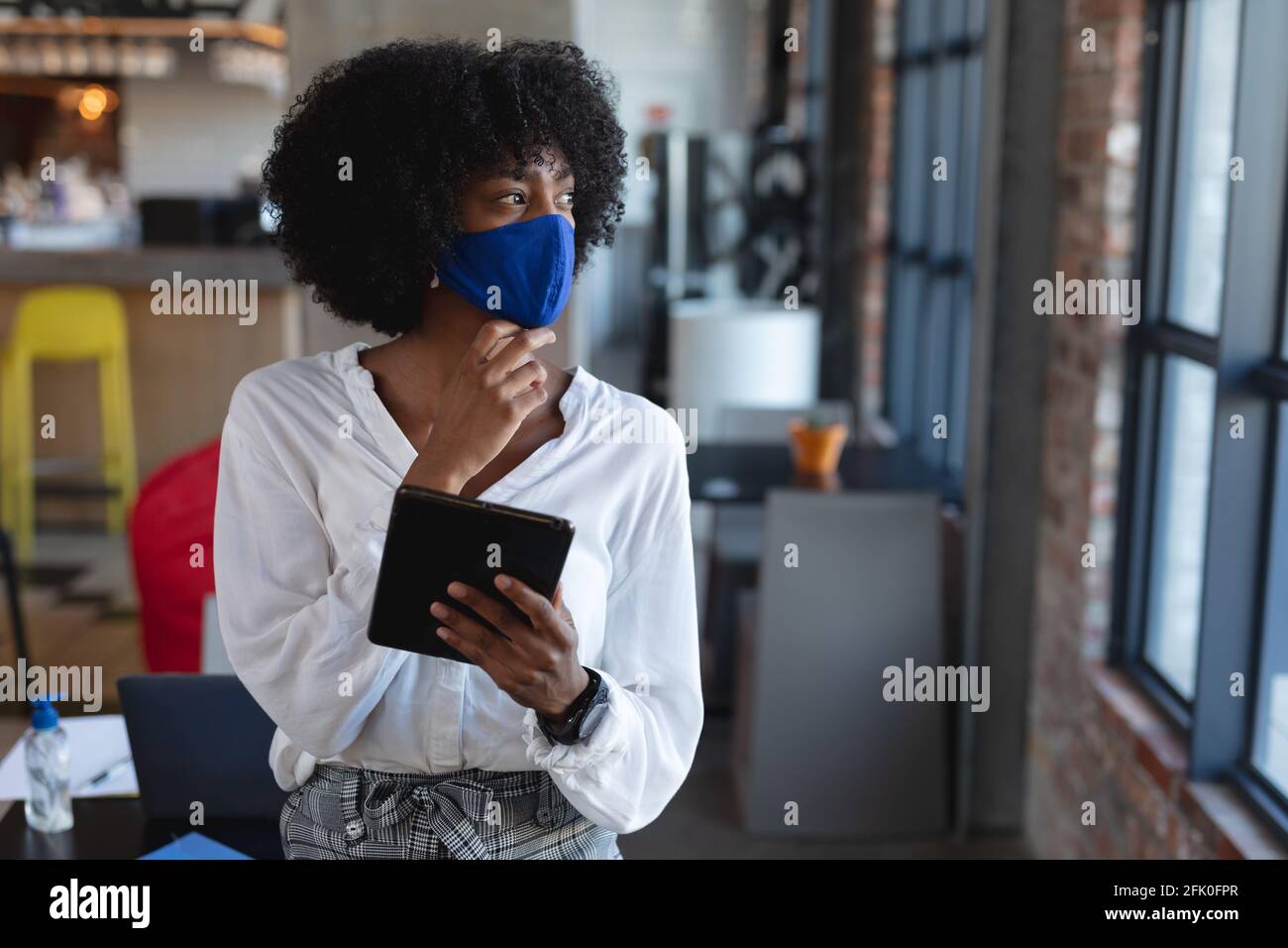 Donna afroamericana che indossa la maschera facciale e che usa la compressa dentro caffè Foto Stock