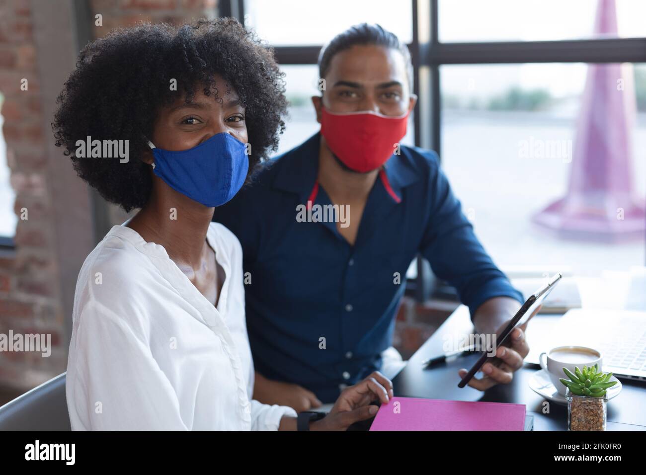 Sorridente razza mista uomo e donna afroamericana indossando maschera seduta, utilizzando tablet in caffetteria Foto Stock