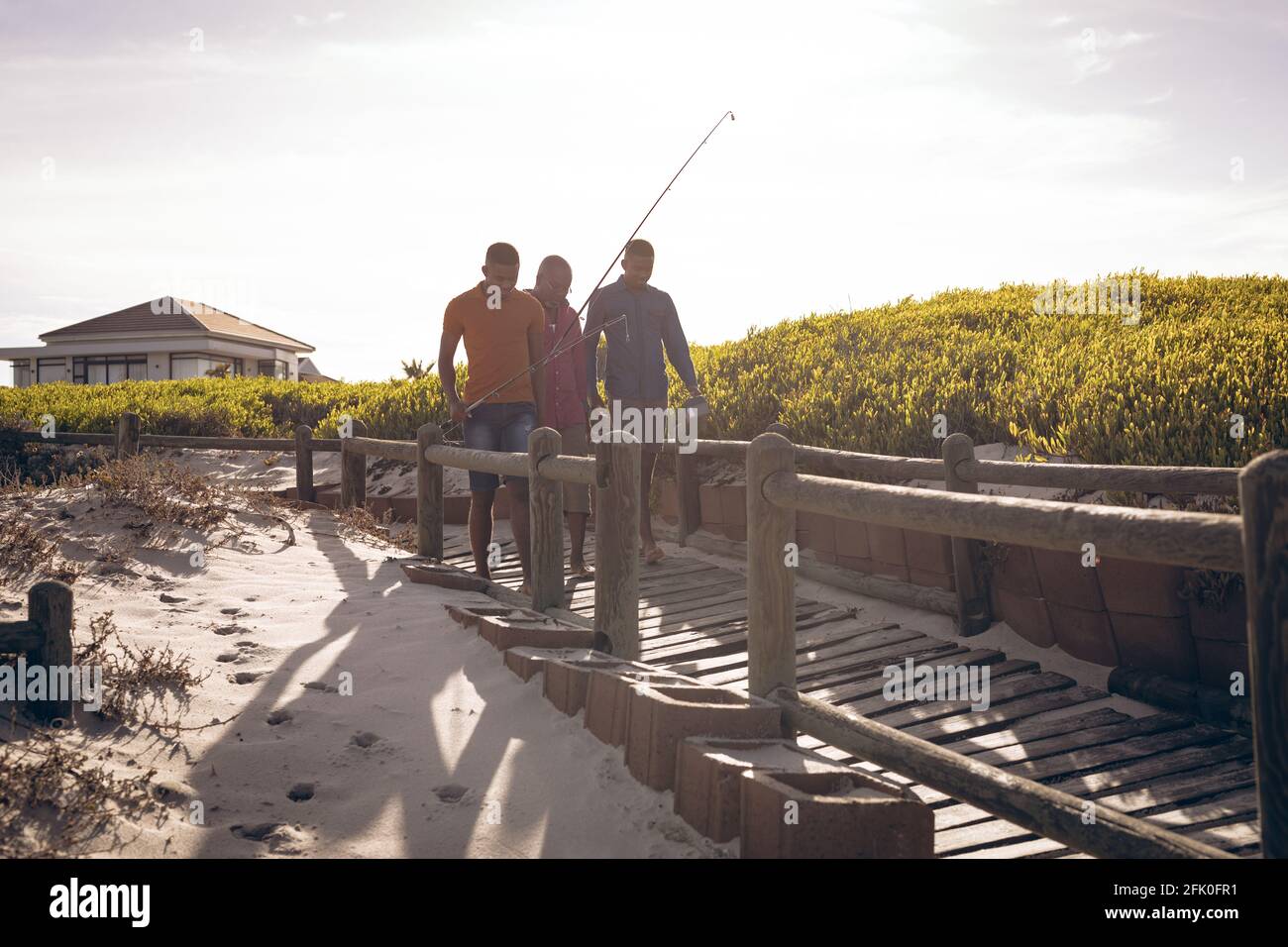 Padre afroamericano e i suoi due figli con canne da pesca camminando insieme sul ponte Foto Stock