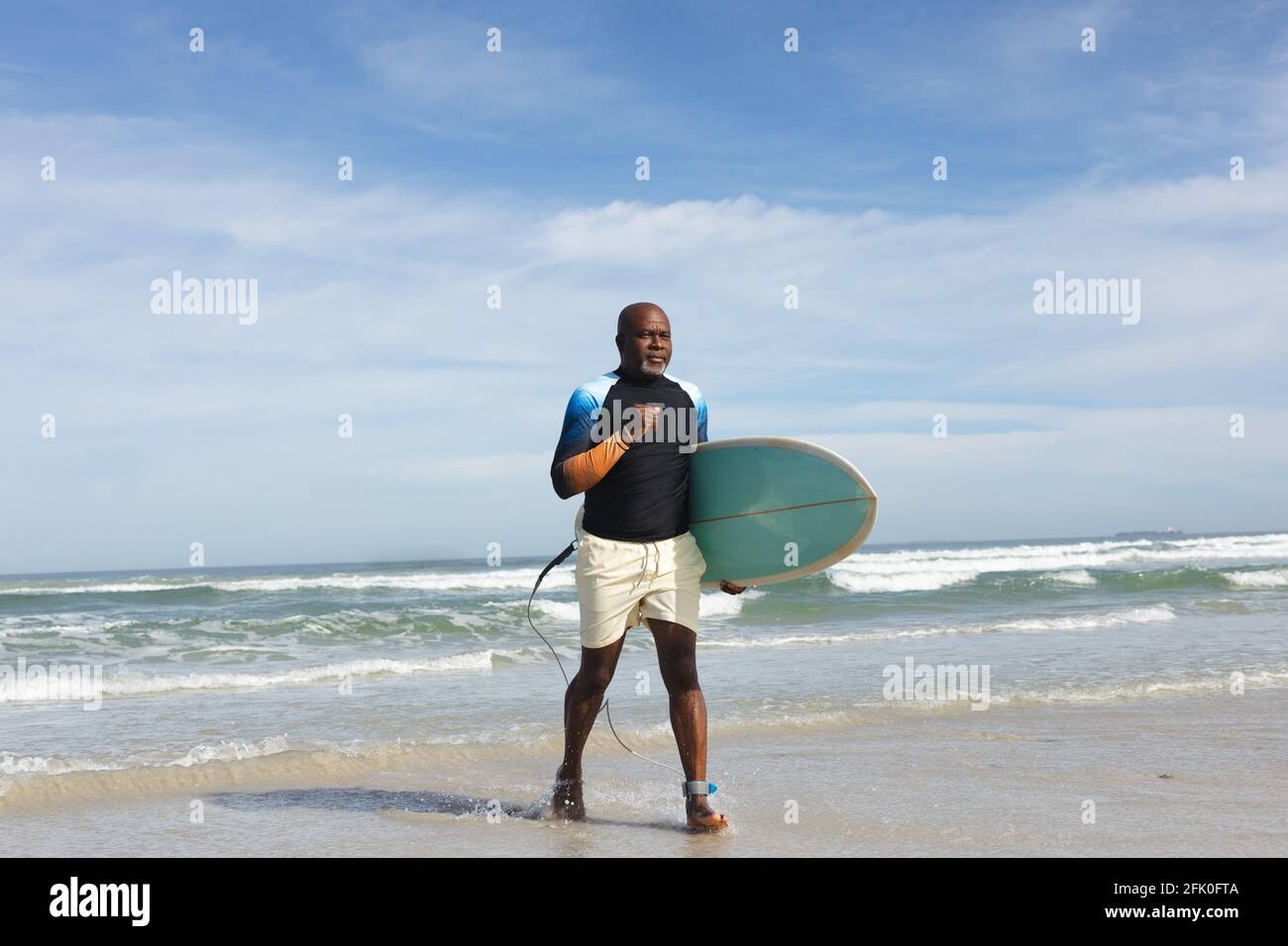 Uomo anziano afroamericano con tavola da surf che cammina verso la spiaggia Foto Stock