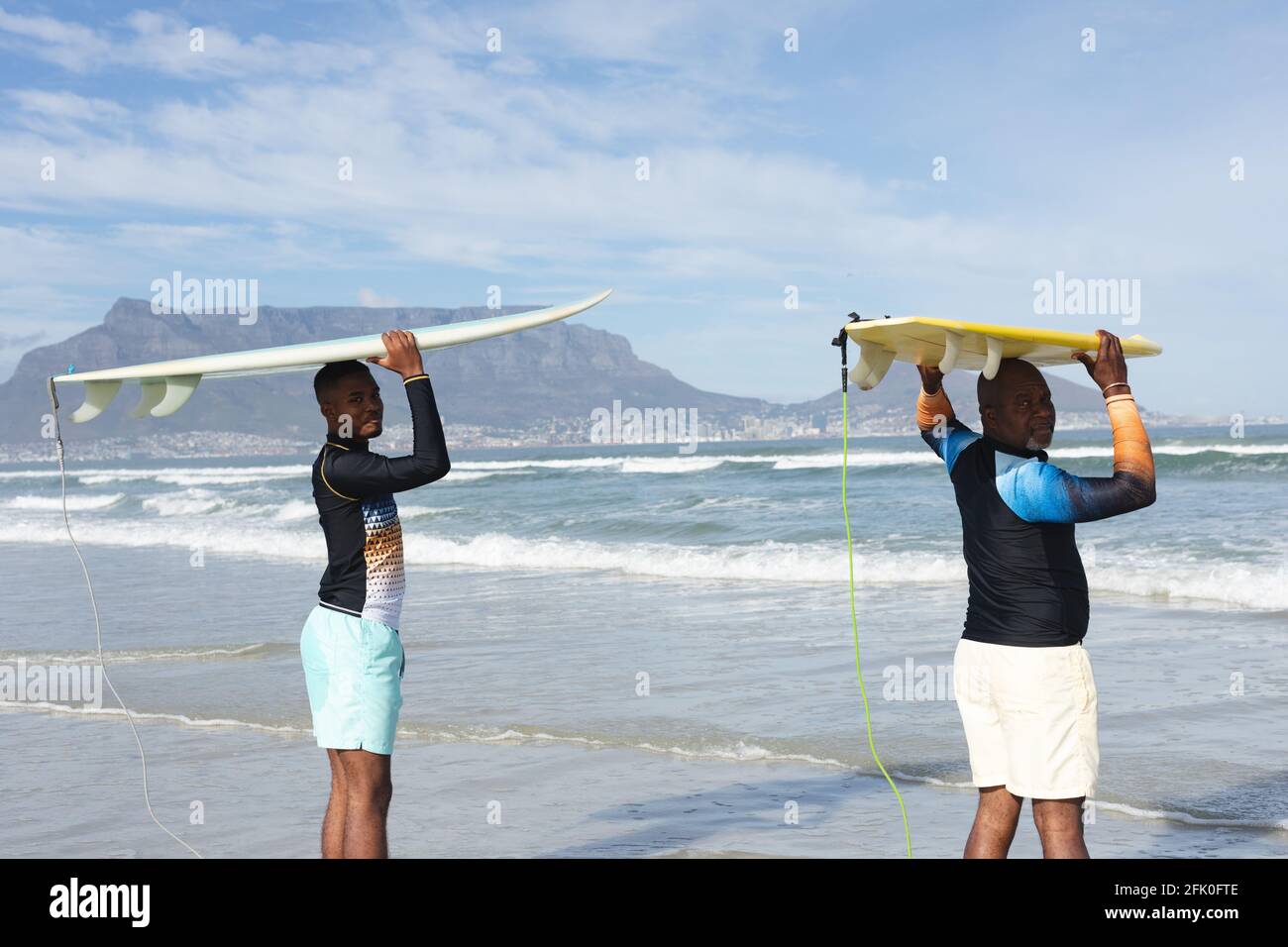 Ritratto di padre e figlio afro-americano che porta tavole da surf la testa in spiaggia Foto Stock