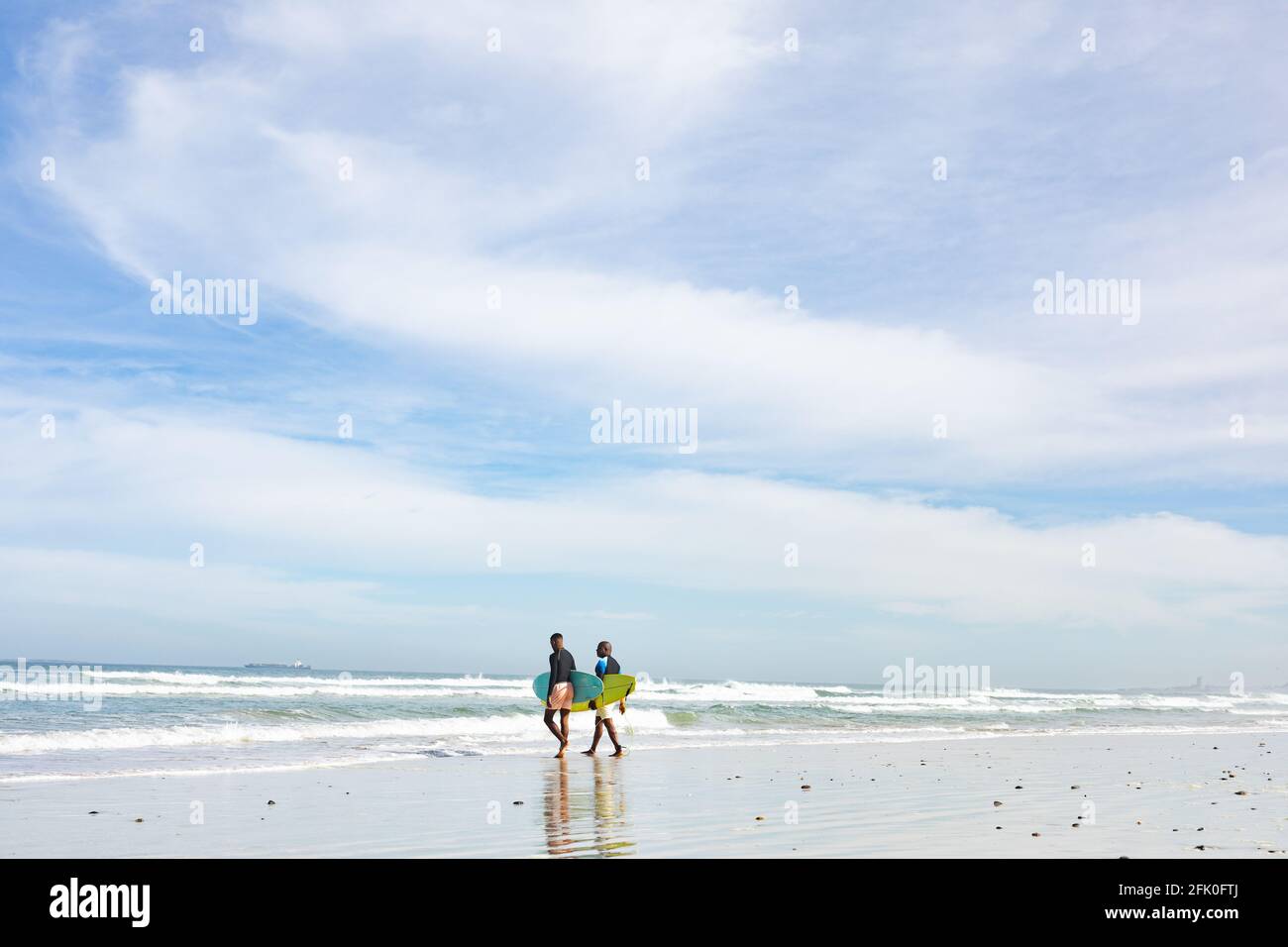 Padre e figlio afro-americano con tavole da surf che camminano verso il onde in spiaggia Foto Stock