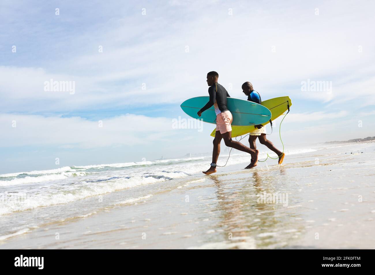 Padre e figlio afro-americano con tavole da surf che corrono verso il onde in spiaggia Foto Stock