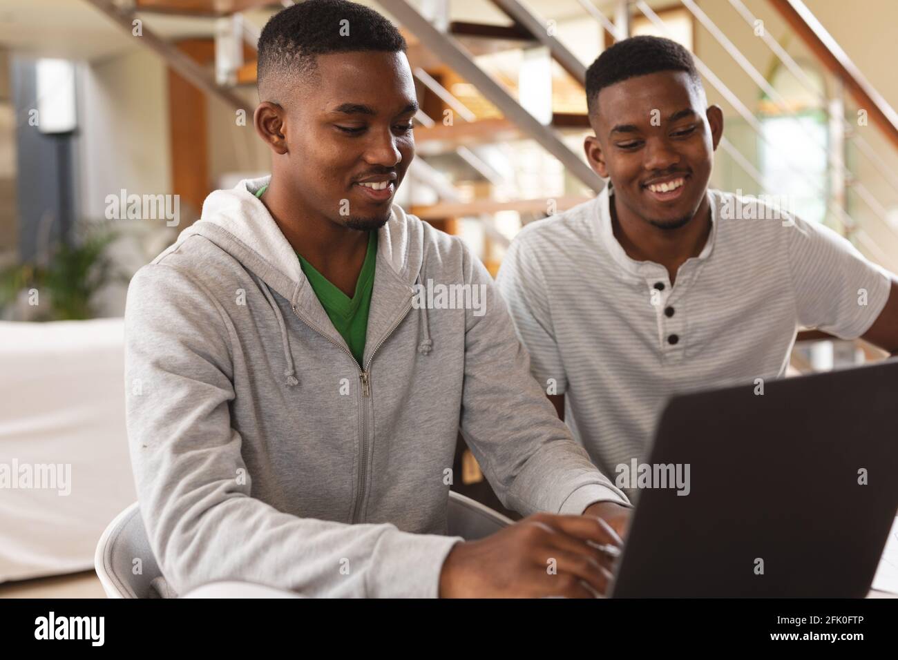 Fratelli afro-americani sorridono mentre usano il computer portatile a casa Foto Stock