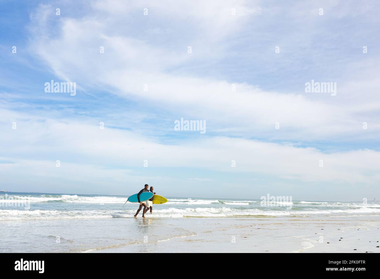 Padre e figlio afro-americano con tavole da surf che camminano verso il spiaggia Foto Stock