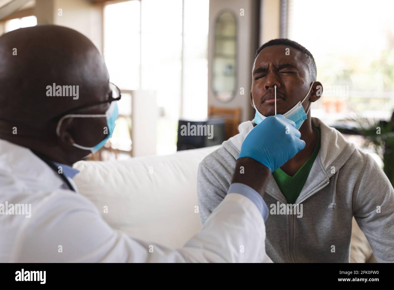 afroamericano Senior maschio medico che esegue il test del tampone nasale su l'uomo afroamericano a casa Foto Stock