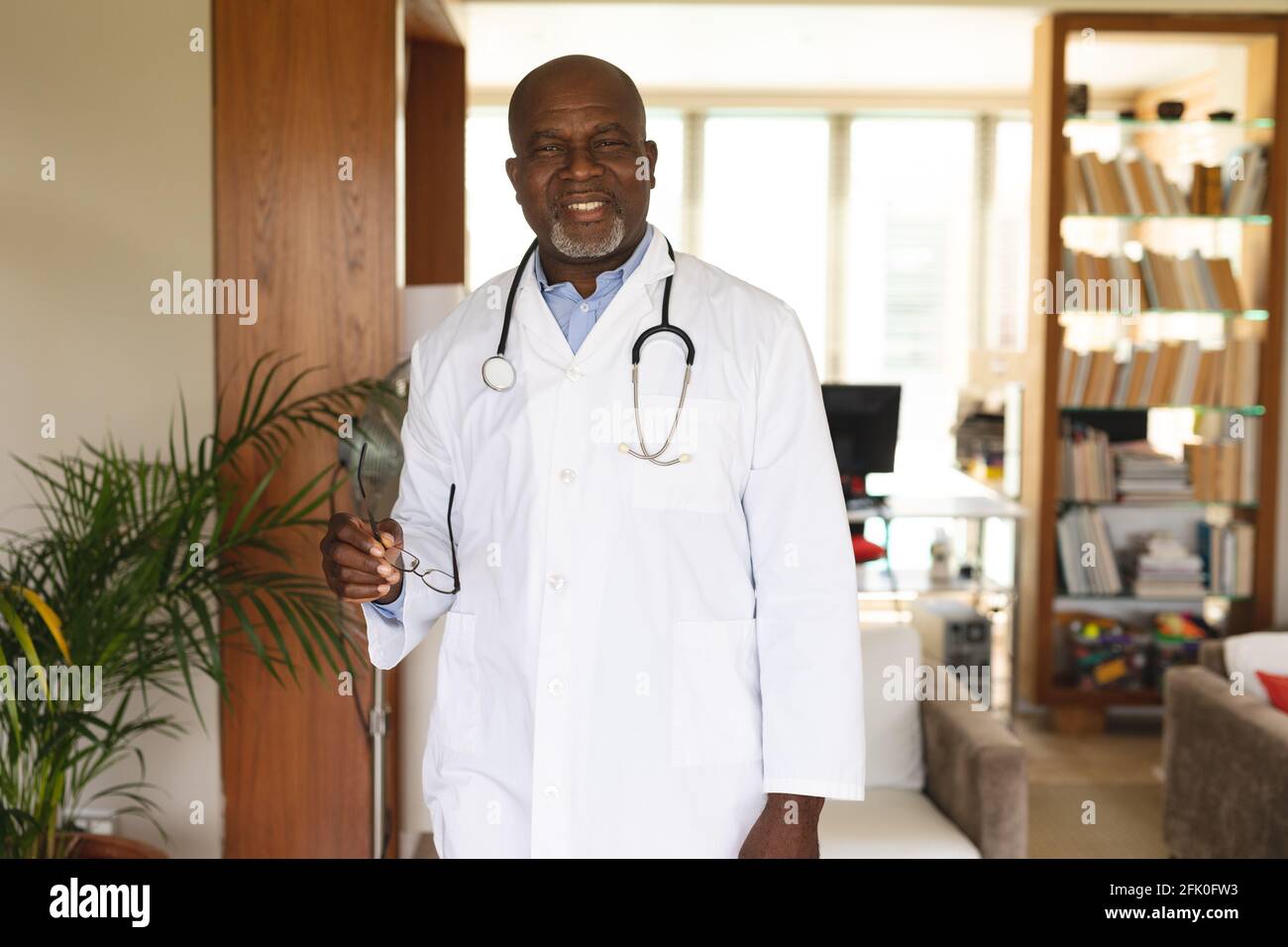 Ritratto di africano americano anziano medico di sesso maschile tenendo occhiali mentre stare a casa Foto Stock