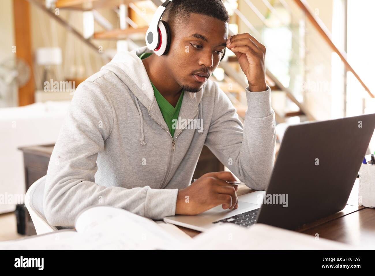 Giovane afro-americano stressato indossando cuffie con laptop mentre studiare a casa Foto Stock