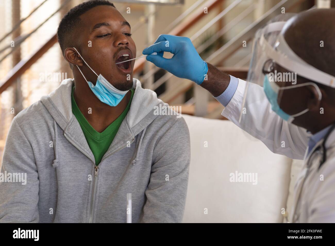 afroamericano anziano medico di sesso maschile eseguendo test di tampone alla gola su l'uomo afroamericano a casa Foto Stock
