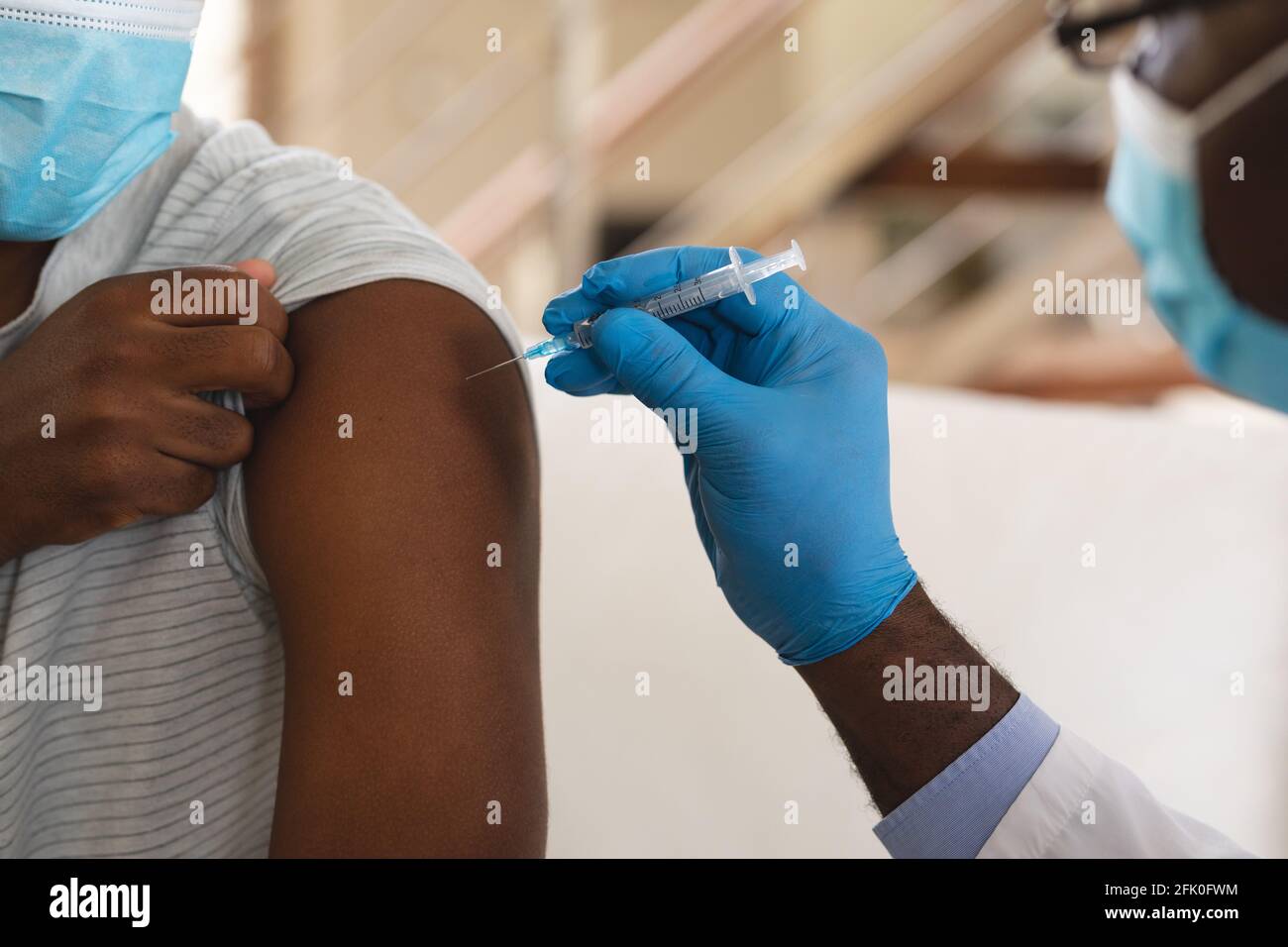 African american Senior Male Doctor iniettando il vaccino covid-19 in africano l'uomo americano a casa Foto Stock