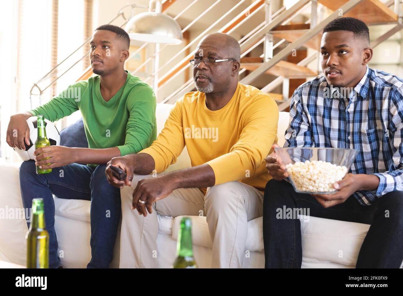L'uomo anziano afroamericano e i suoi due figli che guardano gli sport insieme in tv a casa Foto Stock