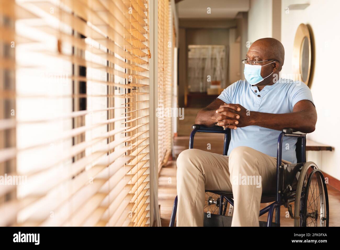 Uomo anziano afro-americano disabile che indossa una maschera seduta la sedia a rotelle a casa Foto Stock