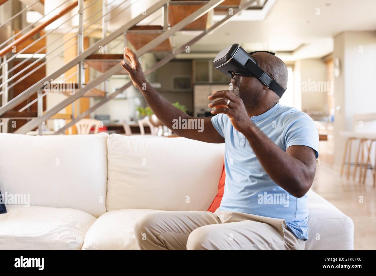 Uomo afro-americano senior gesturing mentre indossa il visore vr seduto sul divano a casa Foto Stock