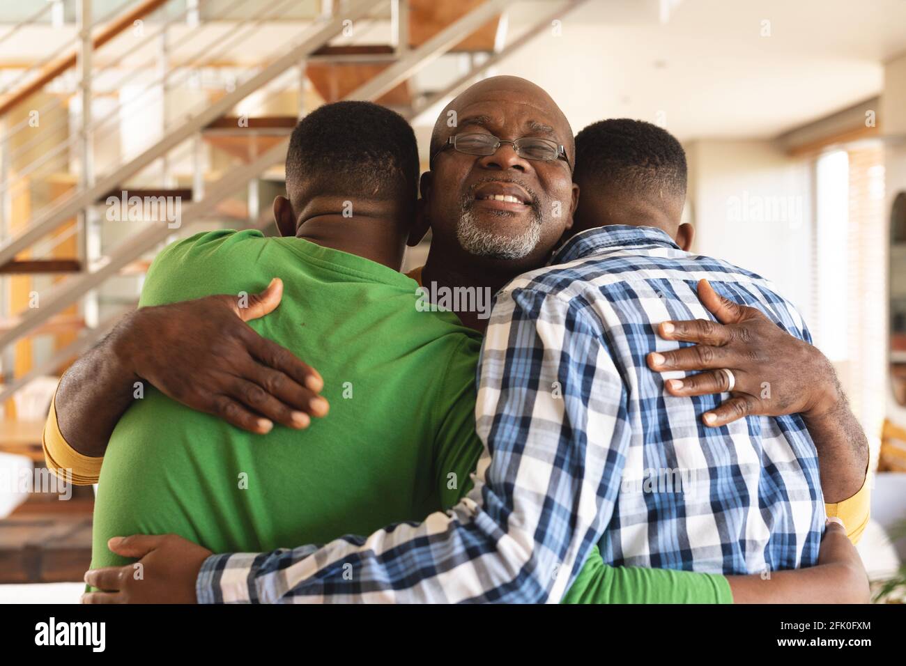 L'uomo anziano afro-americano e i suoi due figli abbracciano ciascuno altro a casa Foto Stock