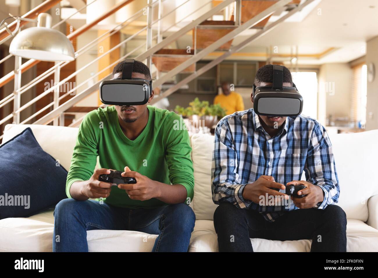Fratelli afro-americani indossano un visore vr mentre giocano i videogiochi seduto sul divano a casa Foto Stock