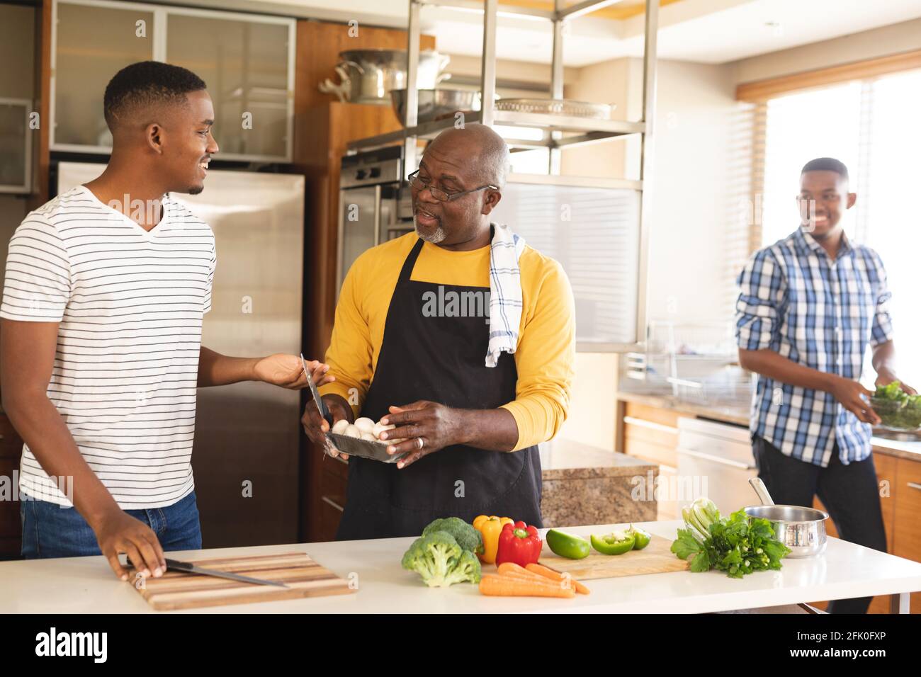 L'anziano afro-americano e i suoi due figli cucinano insieme in cucina a casa Foto Stock