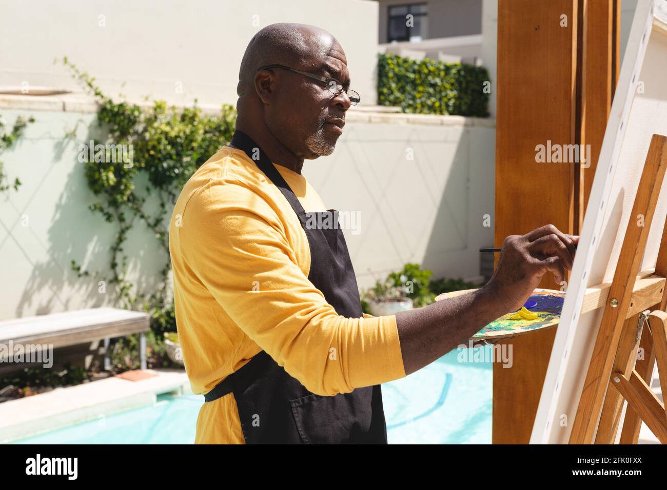 L'uomo anziano afroamericano che indossa la pittura del grembiule su tela vicino la piscina Foto Stock