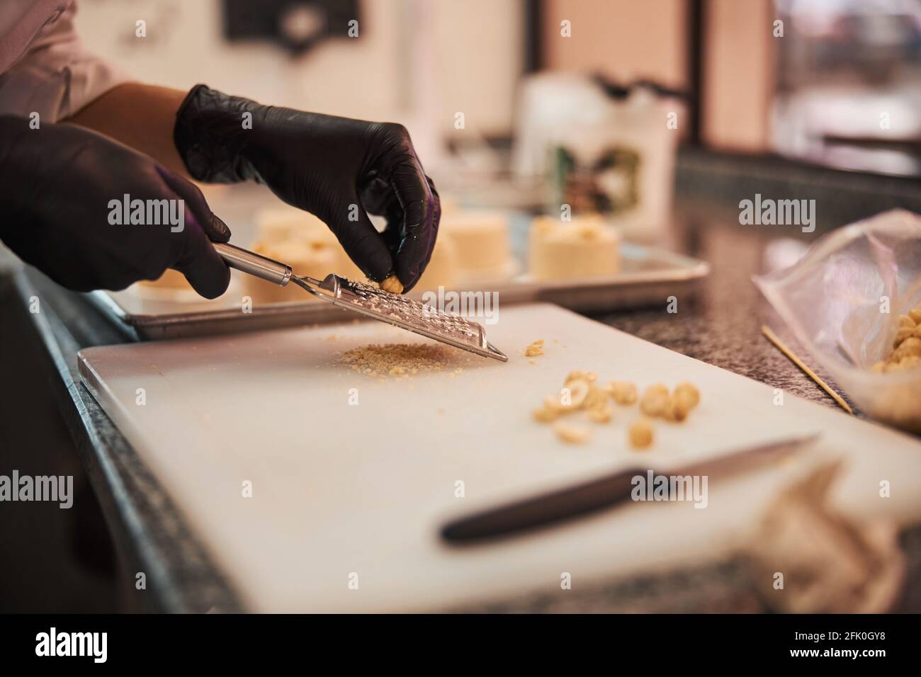 Confettiere qualificato che grattugiano nocciole su un tagliere Foto Stock