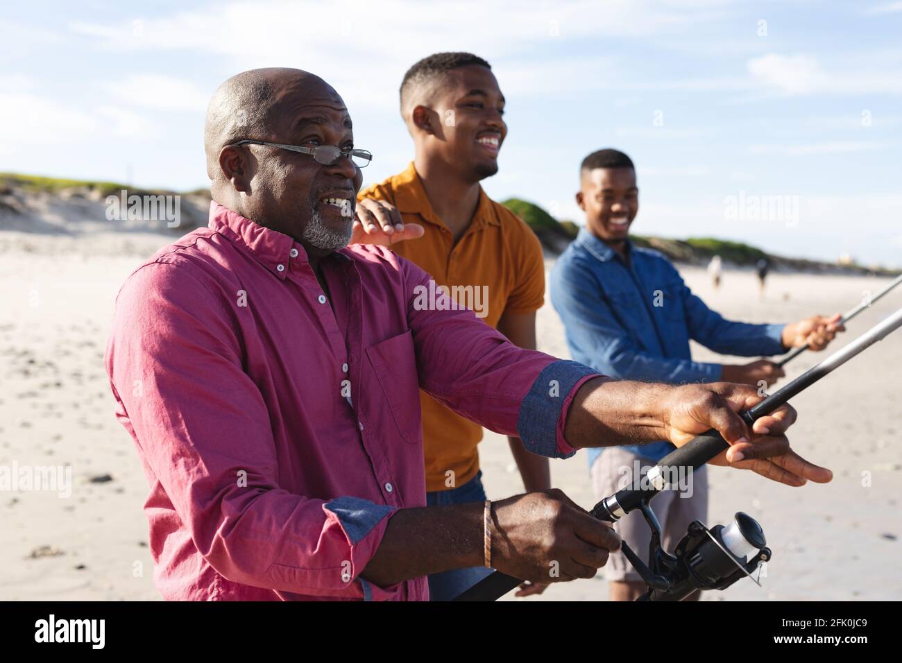 Padre afroamericano e i suoi due figli con canne da pesca pesca insieme in spiaggia Foto Stock